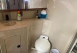 Small bathroom with a white toilet beside a curved beige vanity; cleaning products sit on the counter and a trash can on the floor.