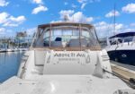 White luxury motor yacht docked at a marina, name 'Above It All' visible on the stern under a blue sky with other boats nearby.
