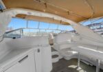 White yacht cockpit with seating, a table, and a sunshade canopy; calm marina visible through windows