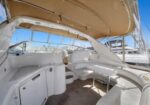White luxury yacht deck with curved seating, a built‑in cabinet, and a beige fabric canopy, at a marina.