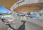 Luxurious white leather seating in a yacht cockpit under a canvas canopy, with a marina and boats visible in the background.