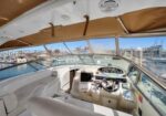Yacht cockpit with white leather seating and helm, harbor and boats in the background outside the windows.