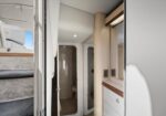 Narrow boat or RV cabin with a small shower stall at the end, bunk bed on the left, and white cabinetry with wood trim on the right.
