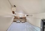 Cozy boat cabin with a double bed, striped bedding, two pillows, and wooden shelves above the bunk window.