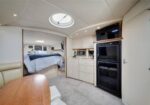 Interior of a luxury boat cabin: sleeping area in the back and a compact galley with microwave, oven, fridge, and cabinets under a round skylight.