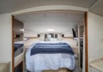 Queen bed in a boat cabin with mirrored side panels, beige wood trim, and a blue-gray quilt draped over the coverlet.