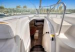 View from the deck into a white motorboat’s cabin; stairs descend to a small seating area with a wooden table, marina in the background.