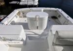 White fishing boat deck with a central bait well, seating on the sides, and a marina in the background.