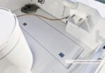 White boat deck with a large central hatch, coiled rope, and a beige hose along the starboard side.
