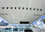 Interior of a bright boat cockpit with a row of ceiling-mounted fishing rod holders, indicating plenty of rod storage; outside view shows houses and marina.