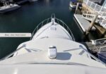 Bird's-eye view of the bow of a white yacht docked at a marina, with calm water and nearby boats visible.