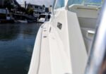 Side view of a white motorboat docked at a marina, with calm water and other boats in the background.