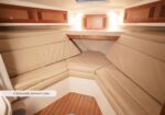 Beige forward cabin on a boat with cushioned L-shaped seating, wooden cabinets above, and a small deck area; label in image reads 'Comfortable forward cabin'.