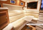 L-shaped beige leather settee with a small white table in a boat cabin, labeled as a pullman sleeper option or bed configuration on the side panel in a yacht interior