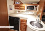 Spacious boat galley for a 35' boat, featuring a compact fridge, wooden drawers, microwave, countertop, and a round stainless sink with faucet.