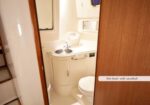 Compact marine head bathroom with a small sink, mirror, cabinet, and toilet visible through a doorway.