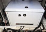 White rectangular Northern Lights 5.1 kW generator in a metal cabinet, with two circular front ports and cables around it in a utility area.