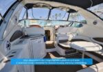 Luxurious yacht cockpit with white seating, a round table, and helm area on a sunlit marina deck.