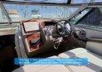 Boat cockpit helm with wooden dash, Garmin display, steering wheel, and beige upholstery at a sunny marina.