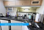 Compact cruise-ship galley with sink, microwave oven, kettle, and assorted appliances along a dark countertop and light wood cabinets.