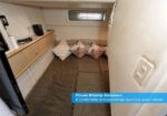 Private midship stateroom on a yacht: compact berth with pillows along a cushioned wall, small window above and built‑in storage.