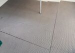 Gray perforated metal floor panels with a single vertical support leg and a small green corner at the edge.