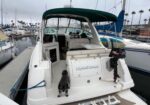 White motorboat docked at a marina with a teal canopy; a small dog stands on the stern.
