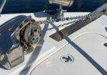 Boat bow with an anchor windlass and chain, showing a metal cleat and deck hatch nearby on calm water.