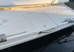 White boat stern deck featuring a rectangular hatch, curved grab handle, and circular vents; water visible below the platform.