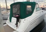 White motorboat with a green canvas cover docked at a marina; stern features an outboard motor and mooring lines visible at sunset.