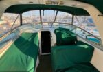 Covered seating area of a motorboat cockpit with green canvas covers and a marina in the background