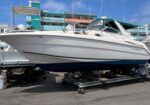 White motor yacht on a wheeled cradle at a marina, with a blue sky and colorful buildings in the background.