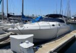 White motor yacht docked at a marina beside other boats and sailboats under a clear blue sky