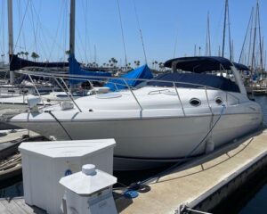 White motor yacht docked at a marina beside other boats and sailboats under a clear blue sky