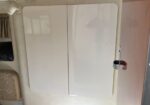 Two white rounded-corner cabinet doors on a beige wall inside a camper or RV storage area. the right door has a brown latch.