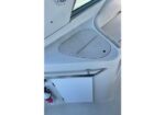 White boat deck with a curved hatch cover (two-panel) and a small circular drainage hole; chrome railing and a white cushioned seat along the edge, with a fire extinguisher visible at lower left.