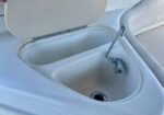 Open boat sink with metal faucet and drain, inside a white fiberglass cockpit with the lid raised.