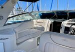 White leather seating area and helm on a luxury boat with blue sky and marina in background.