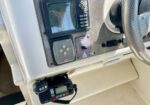 Boat helm with navigation gear: chartplotter screen, control panel, and a VHF radio mounted below; steering wheel on the right.