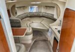 Curved beige seating with patterned cushions inside a small boat cabin, plus a wood table and a compact kitchenette with a sink.