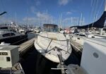 White motorboat docked in a crowded marina with several yachts and masts in a sunny scene.
