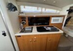 Boat galley with sink, two-burner stove, microwave, and wooden cabinets beneath a curved window.