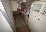 Interior of a small boat cabin: white control panel with switches on the right, storage cabinets, and a red buoy-like object on a rug-covered floor.