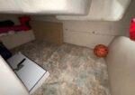 Small, cluttered bunk area with a basketball on the floor near the wall, a clipboard on the floor, and clothes on a shelf.