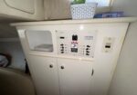 White cabinet with a built-in electrical control panel and multiple switches, an open left compartment, and two doors below; a small basket sits on top.