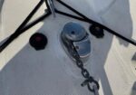 Close-up of a boat anchor windlass with chain on a white textured deck, with lines and cleats nearby.