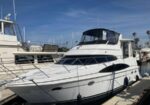 White motor yacht docked at a marina with other boats and a bright blue sky above.