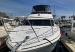 White motor yacht moored at a marina with a dark upper deck cover and blue sky above.