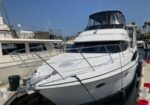 White motor yacht docked at a marina, bow toward the camera with railings and other boats nearby on a sunny day.