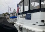 White motor yacht docked at a marina with an American flag; a charter advertisement and phone number are visible on the stern.
